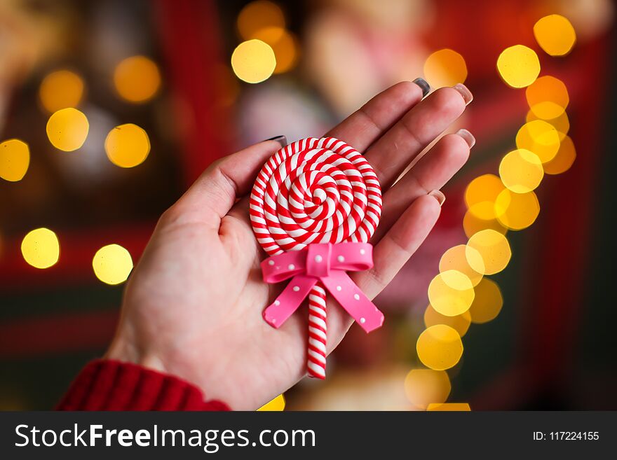 Close up christmas lollipop on woman`s hand on a background of colored lights. Close up christmas lollipop on woman`s hand on a background of colored lights.