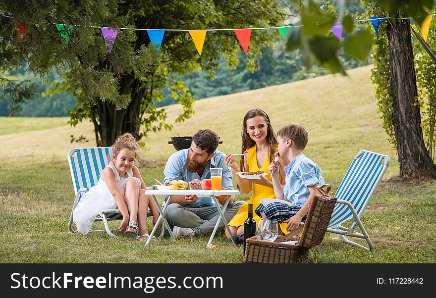 Dedicated young parents of two children listening to their funny son talking while eating together during family picnic in a summer day. Dedicated young parents of two children listening to their funny son talking while eating together during family picnic in a summer day