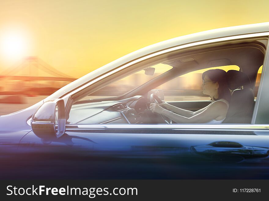 Younger Woman Driving Passenger Car In Urban Against Sunset Sky