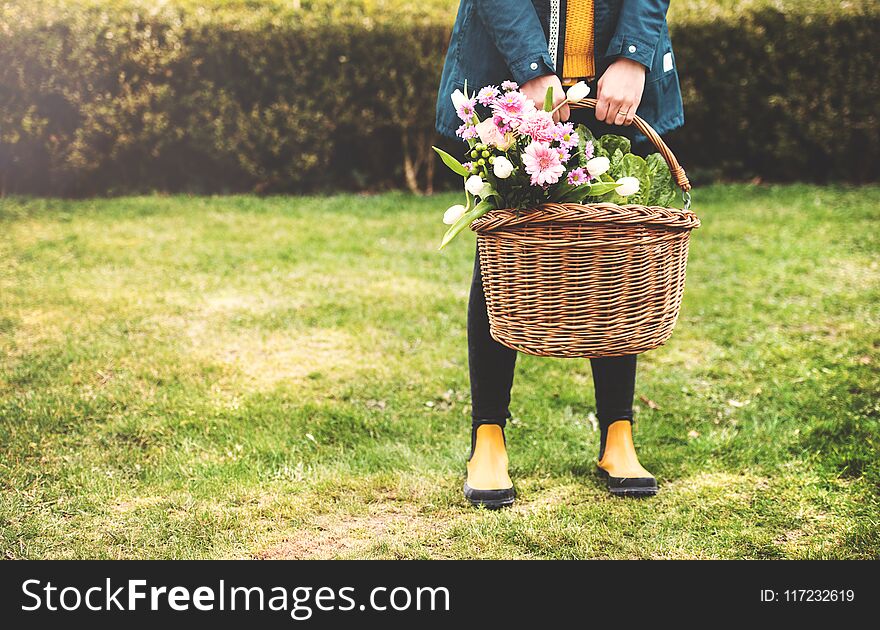 Young woman with flowers in a basket in sunny spring park.