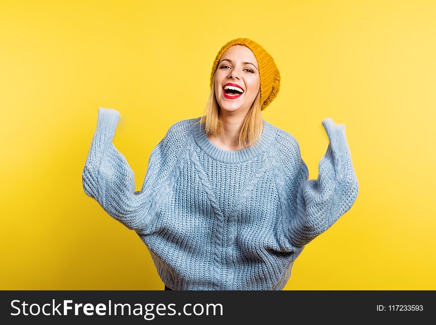 Portrait of a young beautiful woman with a woolen sweater and a hat in studio on a yellow background, having fun. Portrait of a young beautiful woman with a woolen sweater and a hat in studio on a yellow background, having fun.