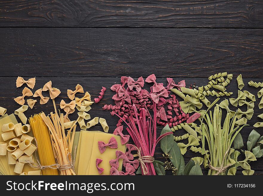Assorted handmade pasta on black wooden background. Colorful tagliatelle with spinach and beetroot juice, farfalle and garganelle - variety of raw italian macaroni, top view, copy space for recipe. Assorted handmade pasta on black wooden background. Colorful tagliatelle with spinach and beetroot juice, farfalle and garganelle - variety of raw italian macaroni, top view, copy space for recipe