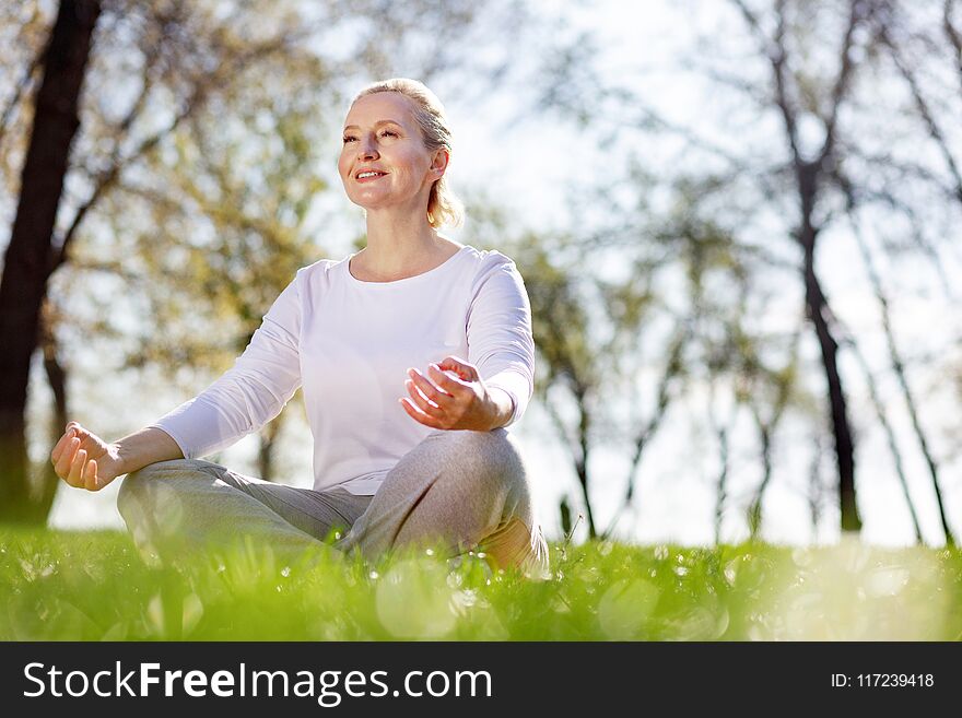 So peaceful. Cheerful peaceful woman sitting in the grass while meditating. So peaceful. Cheerful peaceful woman sitting in the grass while meditating