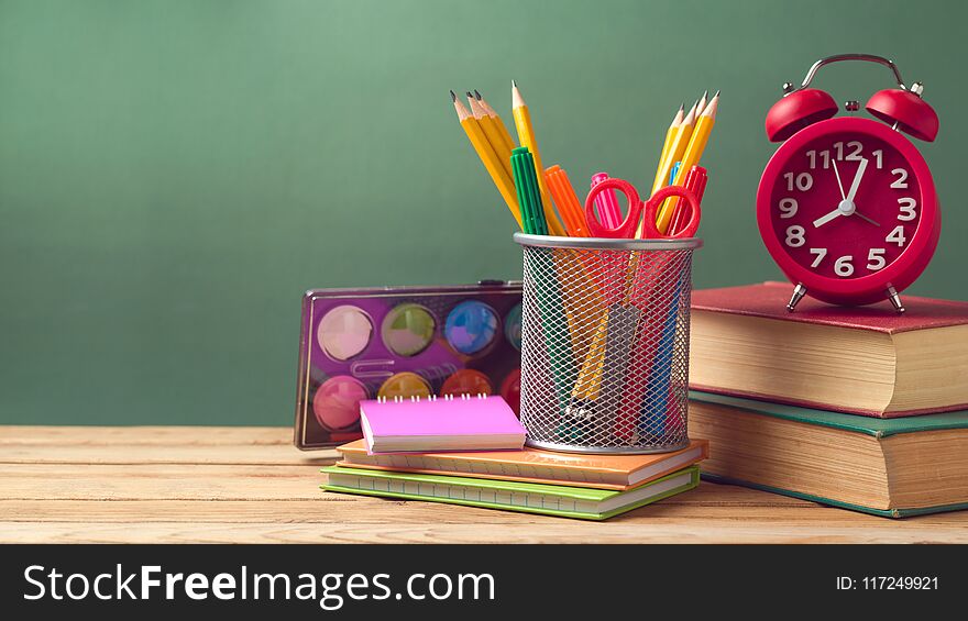 Back to school concept with alarm clock, pencils and old books on wooden table