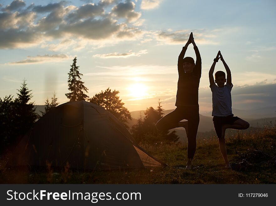 Young mother and son doing gymnastics at the mountains at sunset