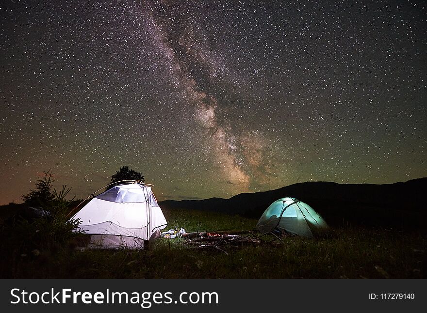 Two illuminated tourist tents at night under incredible beautiful starry sky with Milky way. People hikers having a rest inside tents. Night camping in the Carpathian mountains. Astrophotography. Two illuminated tourist tents at night under incredible beautiful starry sky with Milky way. People hikers having a rest inside tents. Night camping in the Carpathian mountains. Astrophotography