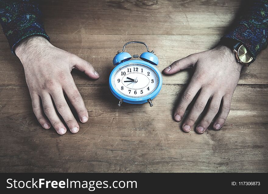 Hands holding blue alarm clock on wooden table.