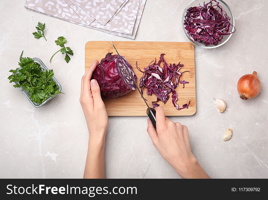 Woman cutting red cabbage on wooden board, top view