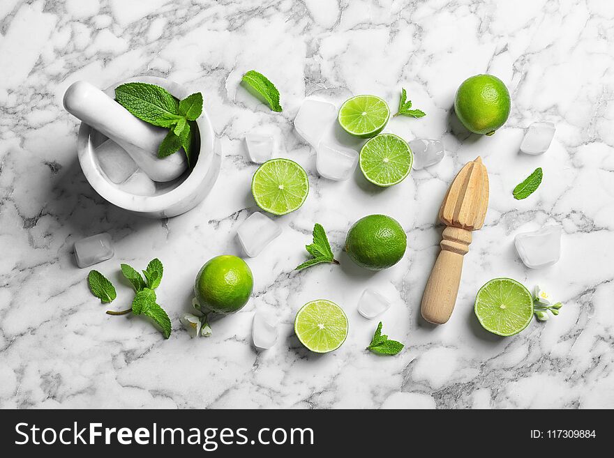 Flat lay composition with lime, juicer and mortar on marble background. Refreshing beverage ingredients