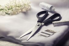 Background With Sewing Tools. Scissors, Bobbins With Thread And Needles And Textile On White Table. Stock Photos