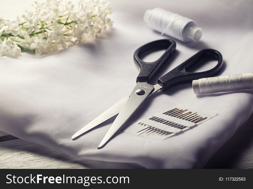 Background with sewing tools. Scissors, bobbins with thread and needles and textile on white table.