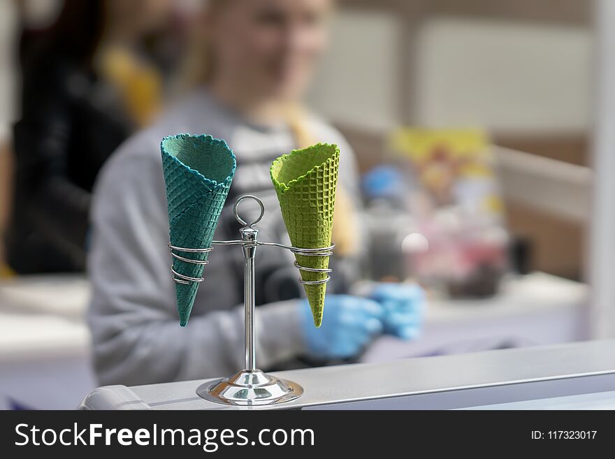 Unrecognizable young saleswoman and two empty bright wafer sweet cornets for ice cream, waffle cones. Selective focus