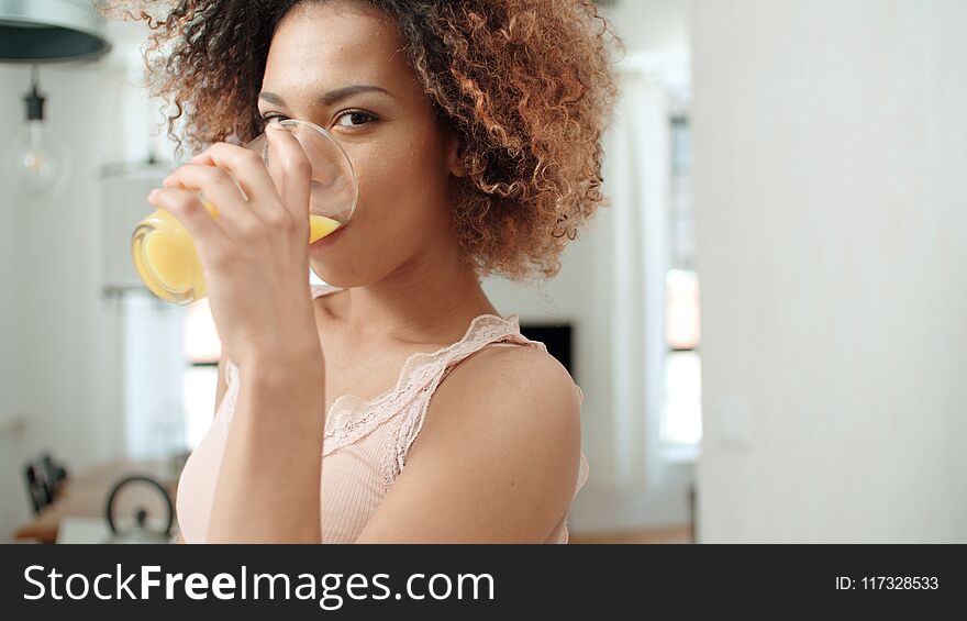 Happy Mixed Race Woman Drinking Orange Juice And Looking To Camera.