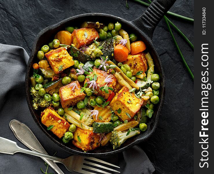 Tofu with vegetables sprinkled with herbs and edible flowers, top view. Vegan dish delicious and nutritious. Healthy eating concept