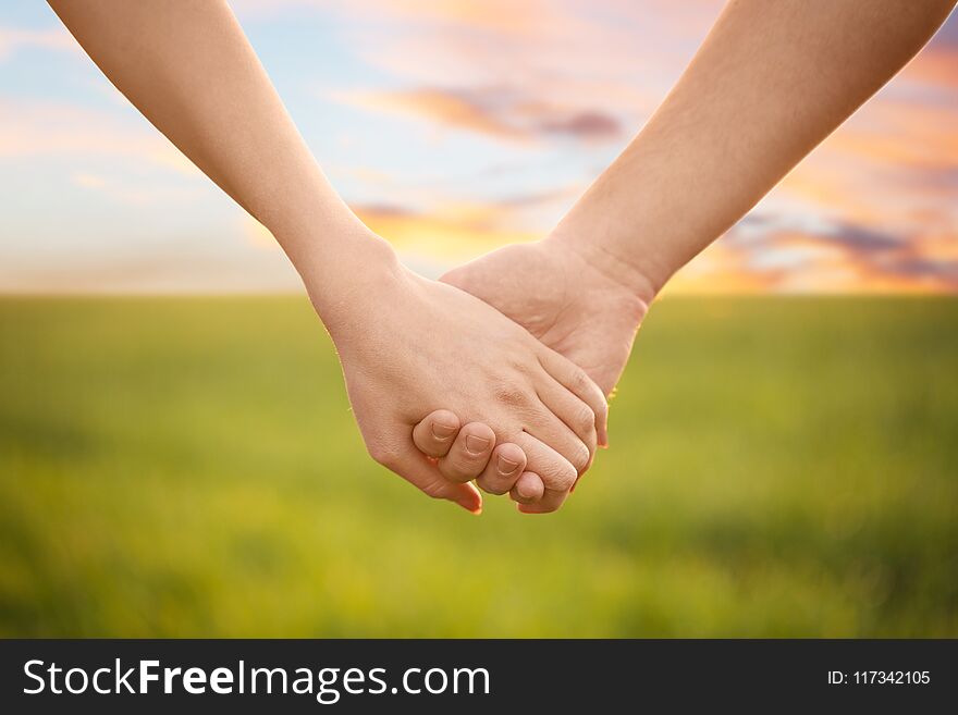 Young lovely couple holding hands in green field, closeup