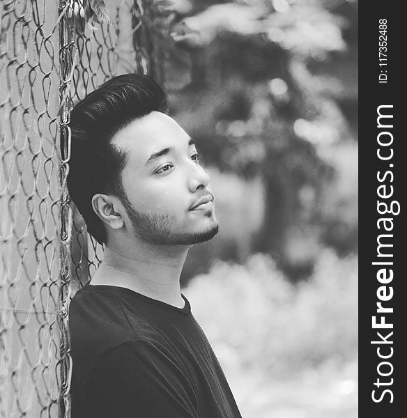 Grayscale Photo of Man Leaning on Wire Fence