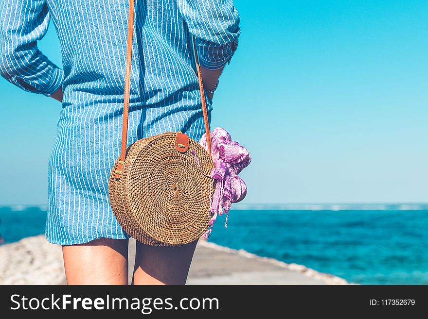 Woman Wearing Blue and White Striped Dress With Brown Rattan Crossbody Bag Near Ocean