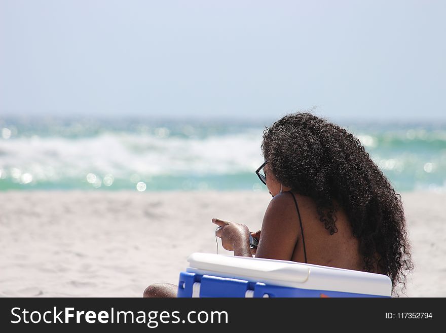 Woman Sitting on Sand Beside Blue and White Cooler Box Near Shore