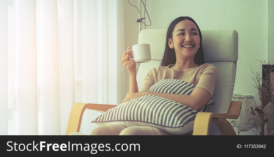 Smile Asian girl on sofa sitting and drinking coffee by the windows