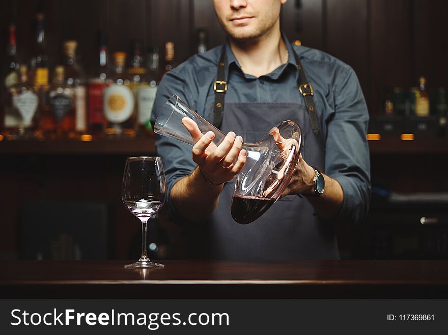 Sommelier pouring wine into glass from decanter. Male waiter pour out alcohol beverage into wineglass at bar counter. Bartender at work. Sommelier pouring wine into glass from decanter. Male waiter pour out alcohol beverage into wineglass at bar counter. Bartender at work