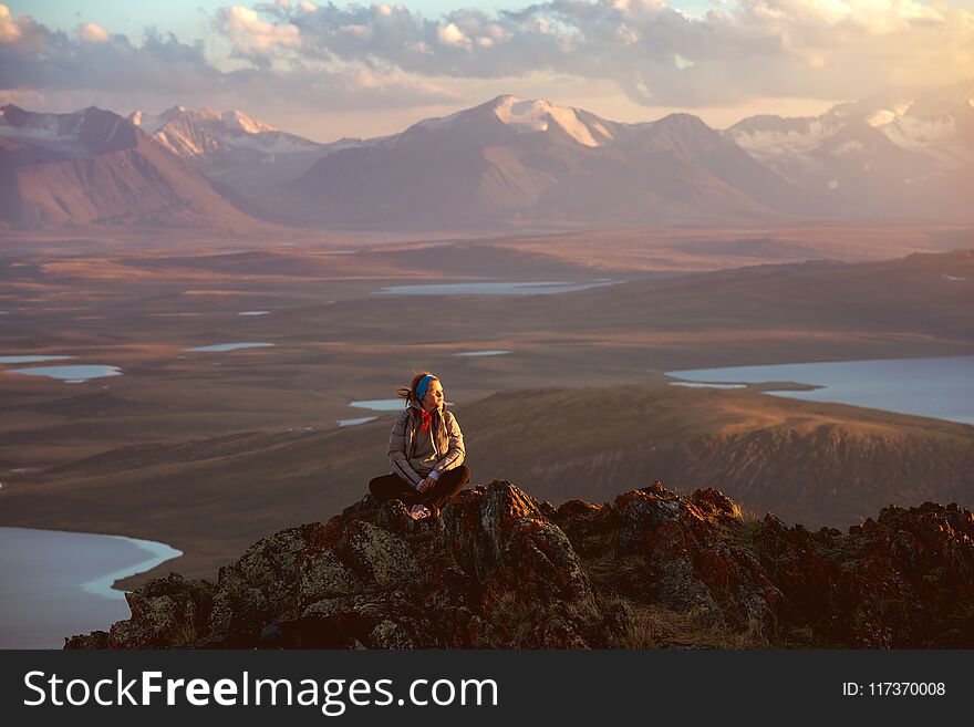 Girl sits and having rest on big rock at mountain top against mountains and lakes valeey. Girl sits and having rest on big rock at mountain top against mountains and lakes valeey
