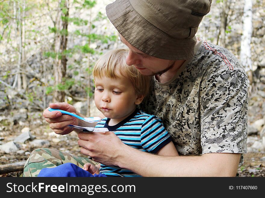 Father Feeding His Son With A Spoon Outdoors