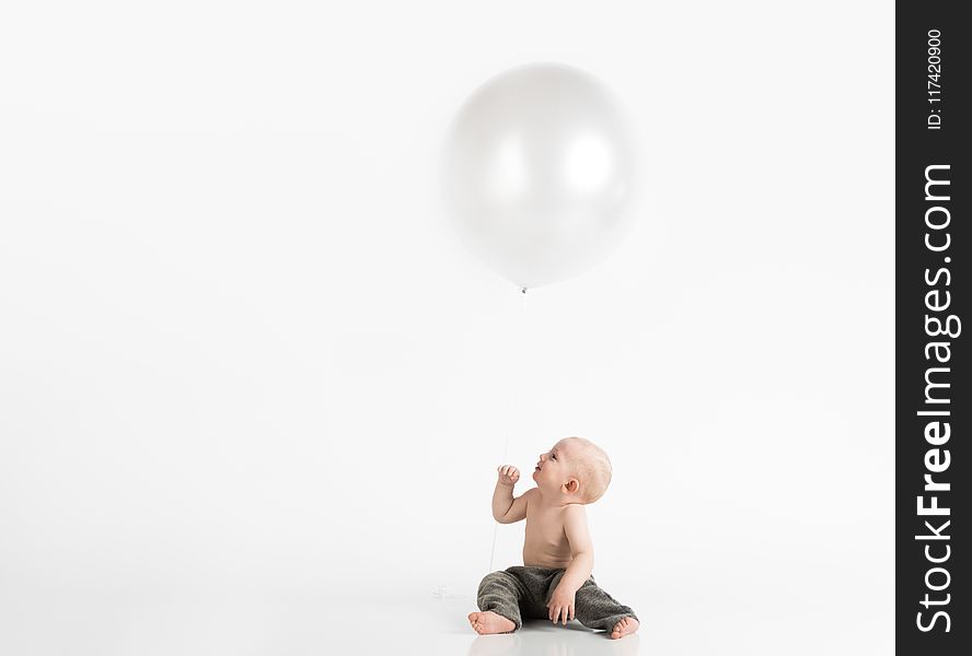 Topless Toddler With Pants Sitting on White Surface While Looking Up