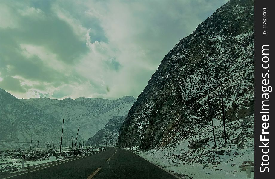 Snow Covered Mountain Ranges Near The Asphalt Road Under The Cloudy Sky