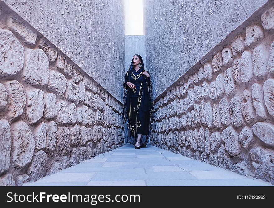 Woman in Black and Gold Traditional Dress Between Gray Concrete Walls