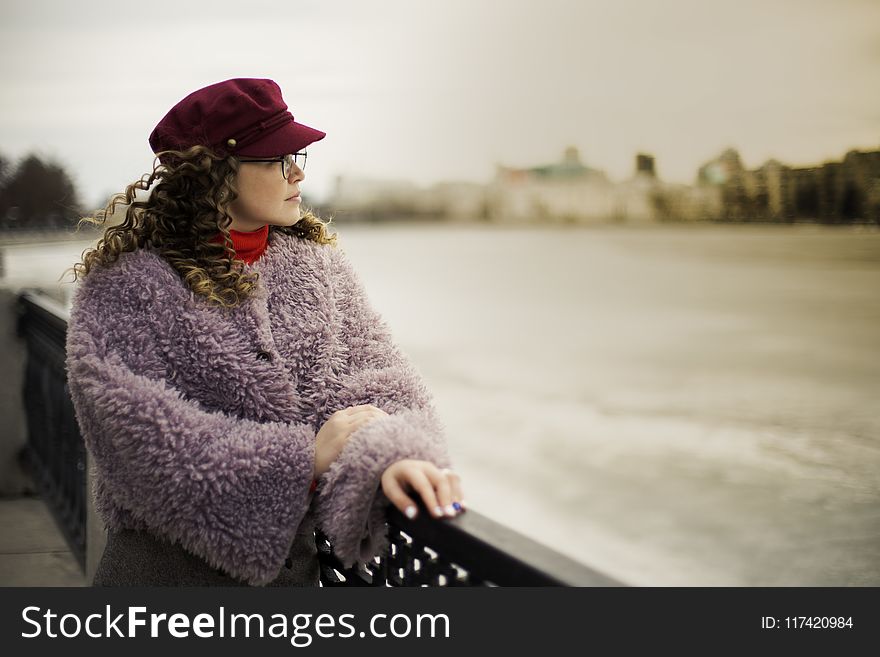 Woman Wearing Purple Fleece Coat Standing Beside Black Metal Fence Near Body of Water