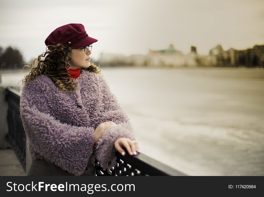 Woman Wearing Purple Fleece Coat Standing Beside Black Metal Fence Near Body Of Water