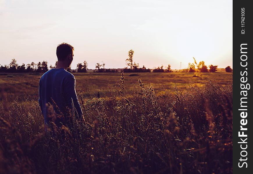 Man In Blue Sweatshirt In The Middle Of Field During Sunset