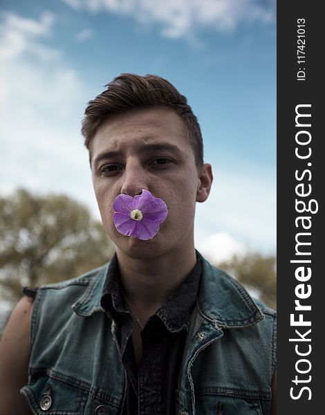 Man in Blue Denim Collared Vest With Purple Flower on Mouth