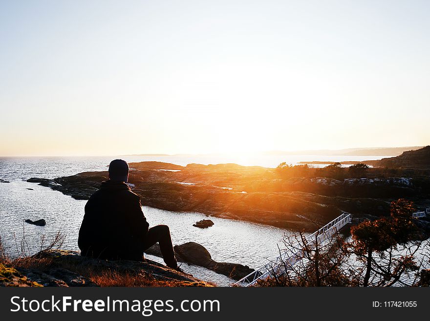 Silhouette Photo of Person Sitting Near Cliff during Golden Hour
