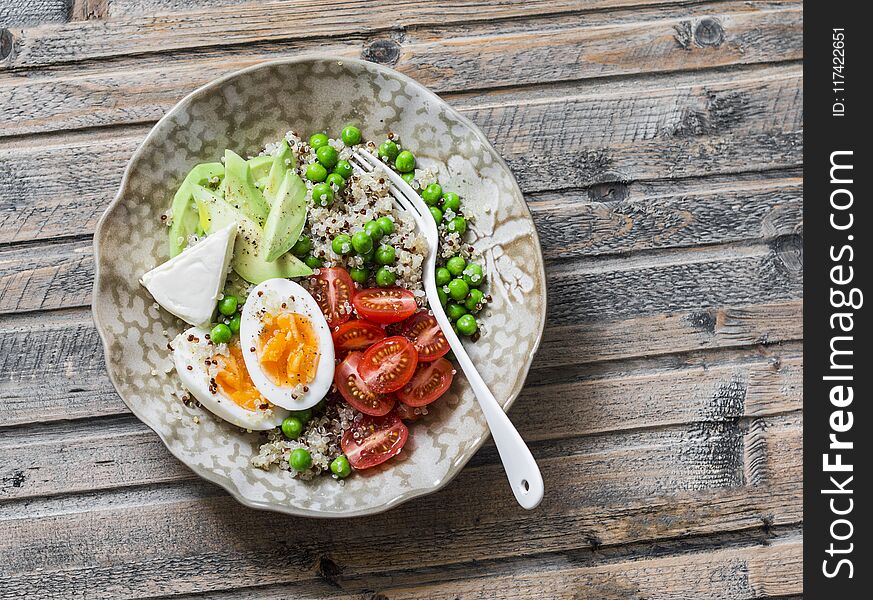 Bowl with quinoa, egg, avocado, tomato, green pea. Healthy diet food concept. Top view, on wooden background