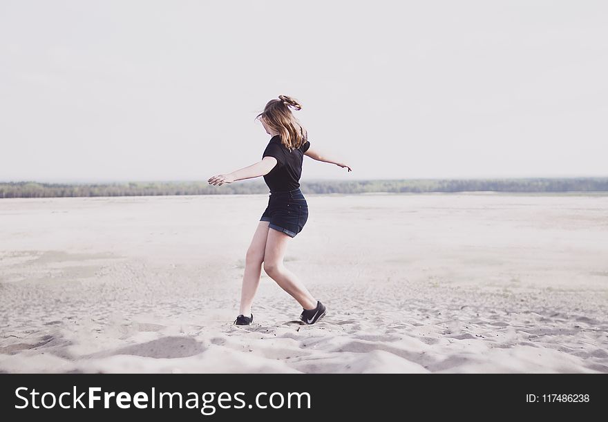 Woman In Black T-shirt And Black Denim Shorts Walking On Sand