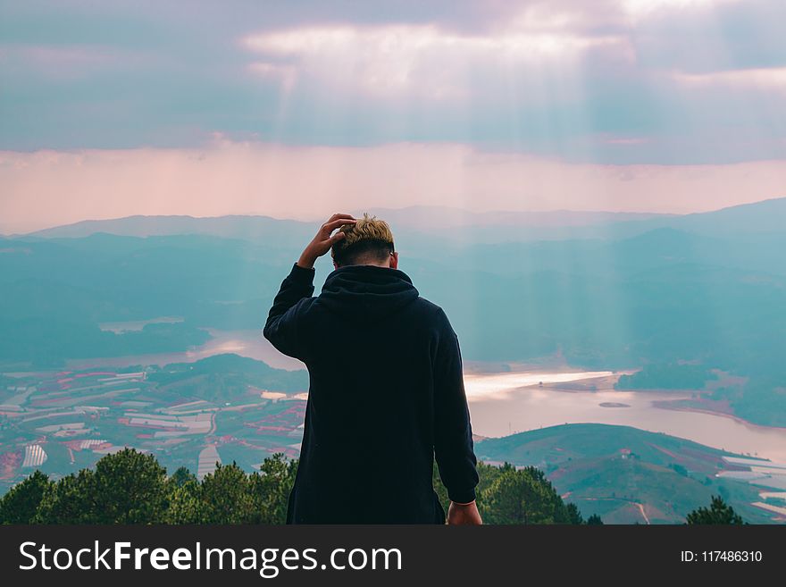 Man in Black Jacket Holding His Hair Facing Body of Water