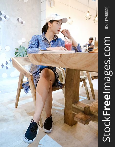 Woman Sits On Brown Wooden Chair Near Brown Table Inside Room