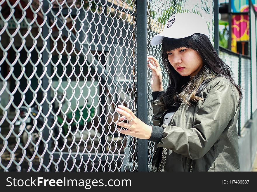 Woman Wearing Grey Bomber Jacket Leaning Near Grey Wire Fence