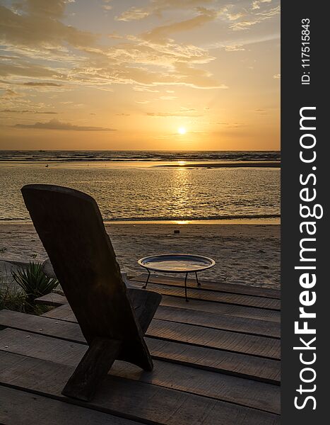 Traditional wooden African chair on terrasse at beach overlooking the ocean during beautiful sunset, Senegal, Africa.