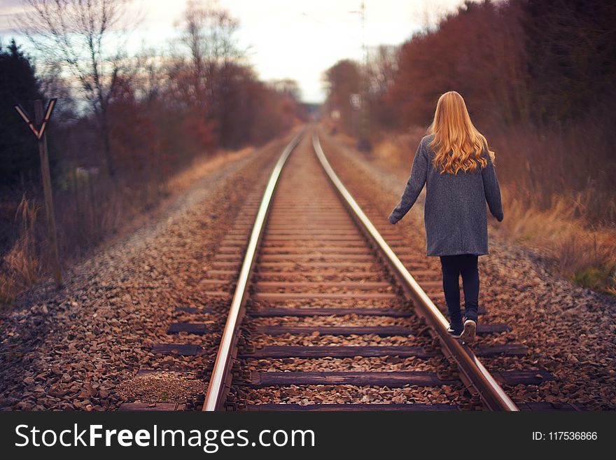 Woman in Blue Jacket and Blue Jeans Walking on Train Track Photography