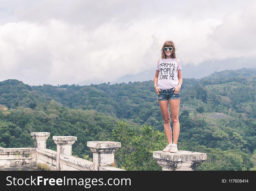 Woman Wearing White Shirt and Blue Denim Shorts Standing on Gray Concrete Stand