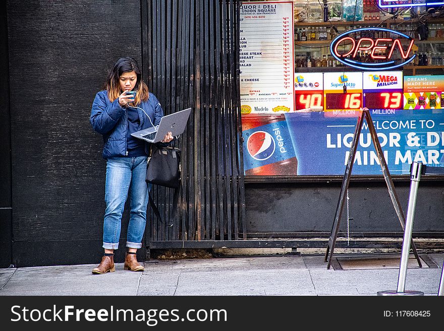 Woman in Blue Jeans Holding Macbook Pro Standing Against Black Wall