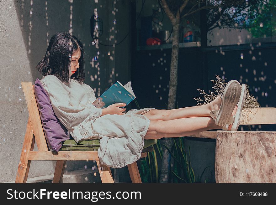 Woman Sitting On Chair While Reading Book