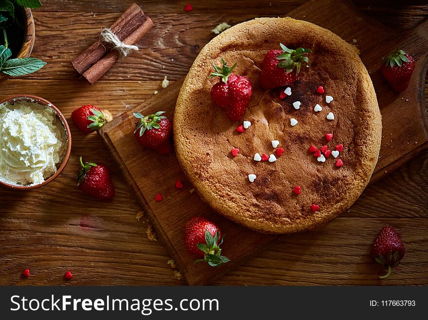 Delicious cake with fresh organic strawberries and kitchen utensils, top view, close-up, selctive focus. Sweet homemade dessert surrounded by natural ingredients on wooden table. Rustic background. Tasty morning pastry. Homemade food concept.