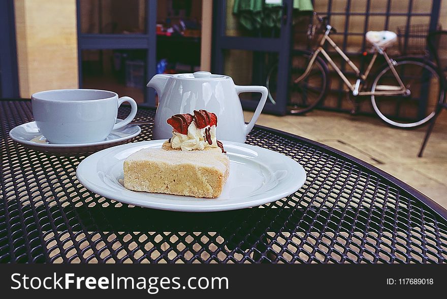 Cake on Ceramic Plate Near Teapot and Cups