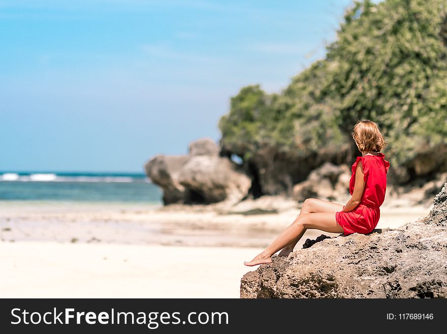 Woman in Red Dress Sitting on Brown Rock