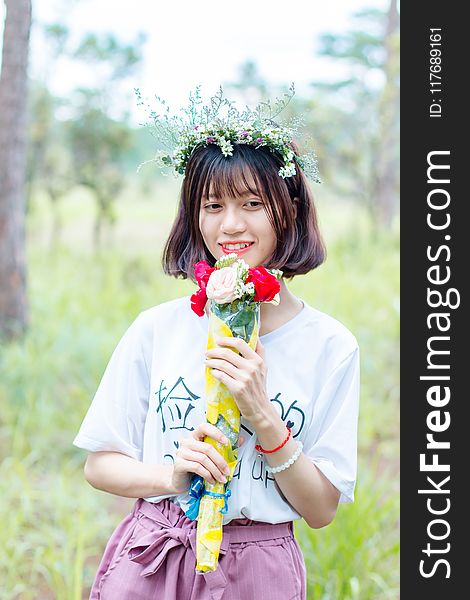 Woman Wearing White Shirt And Purple Bottoms Holding Bouquet Of Flowers