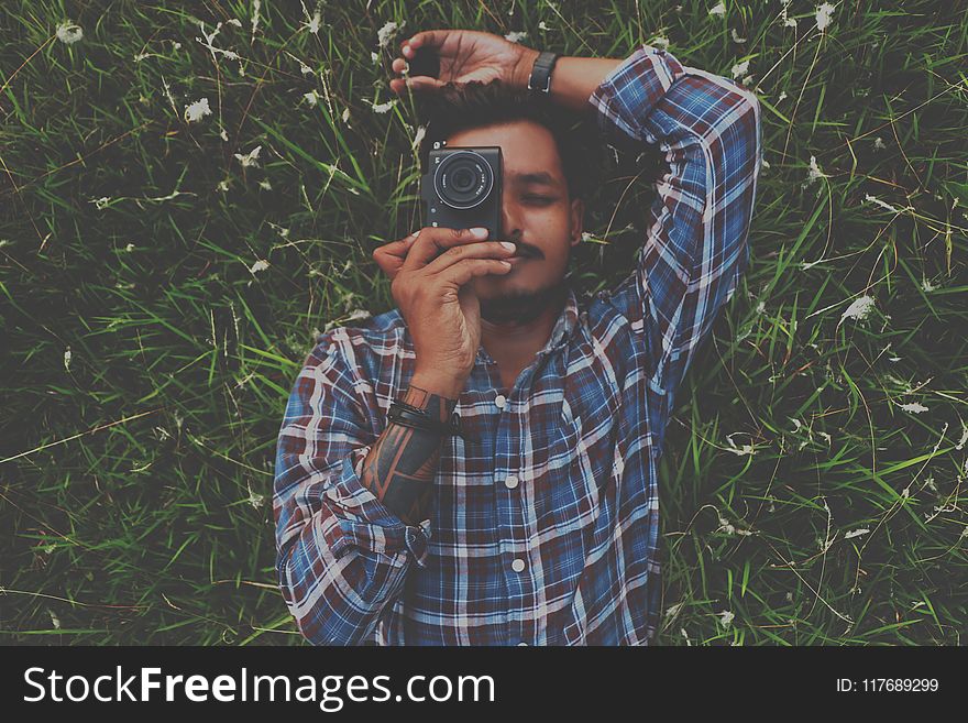 Man in Blue Dress Shirt Holding Camera White Laying on Grass