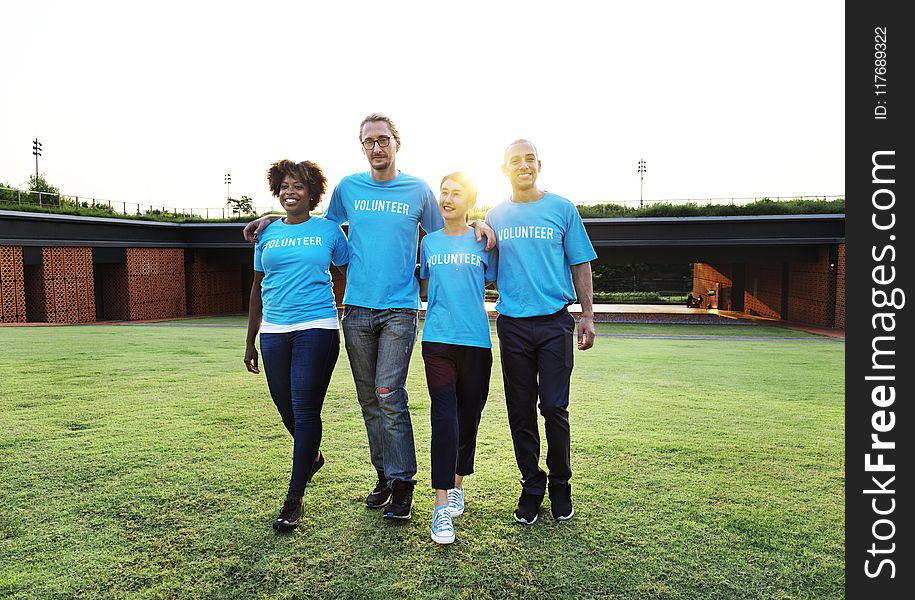 Four People Wearing Blue Crew-neck Shirts Standing on Lawn